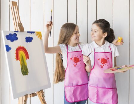 portrait-smiling-two-girls-pink-apron-making-fun-while-painting-canvas (1)